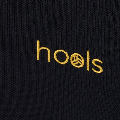 Detalle del logo bordado Hools en polo negro con rayas amarillas